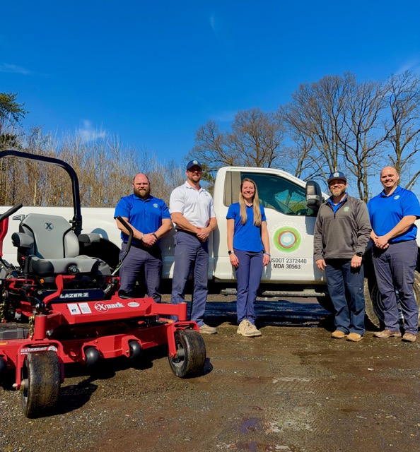 Team posing with lawnmower and truck outdoors.